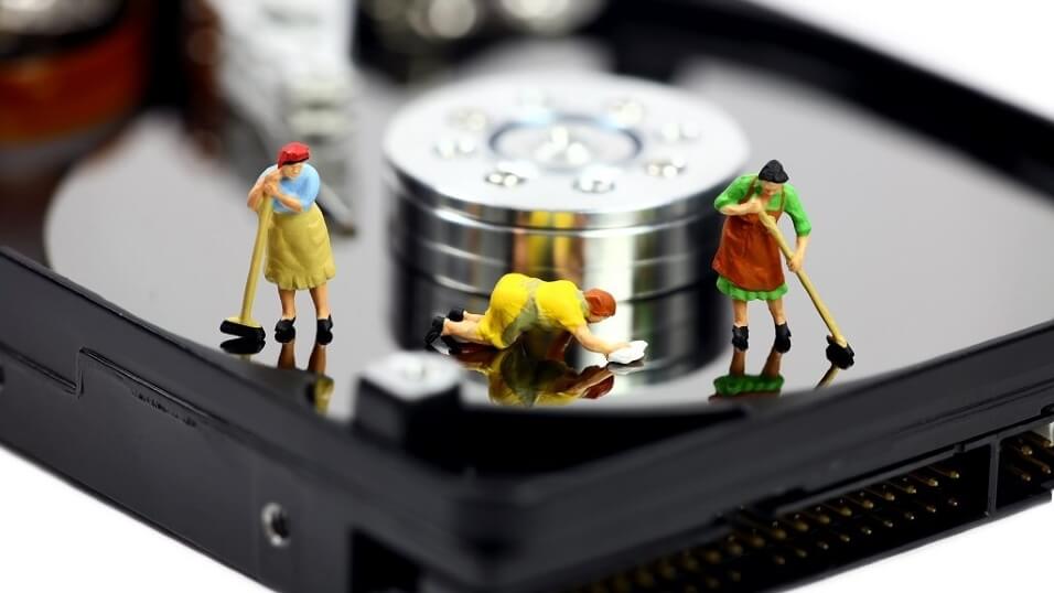 close up view of a hard disk drive with little plastic figures on it. They represent cleaners and they are sweeping and cleaning the hard drive