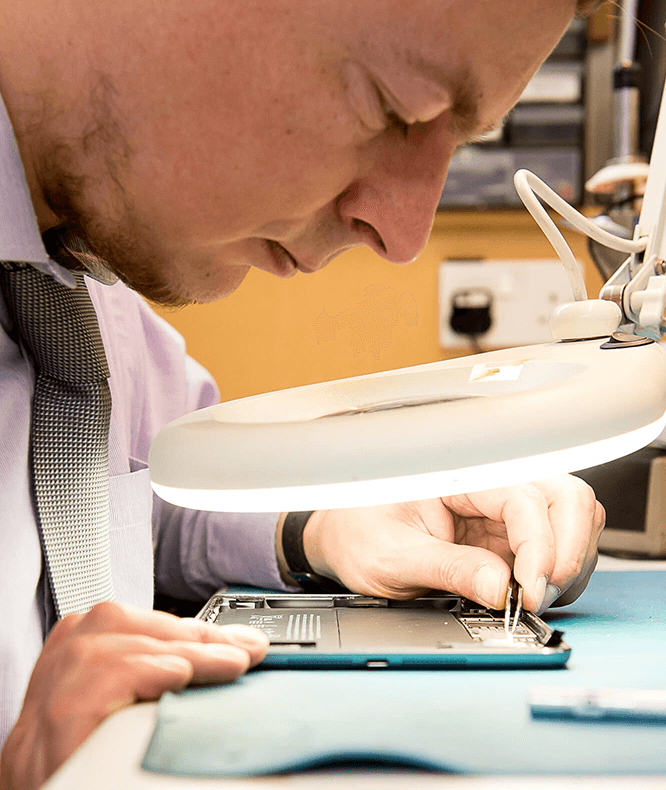 a SimplyFixIt technician fixing an iPhone under a light with magnification.